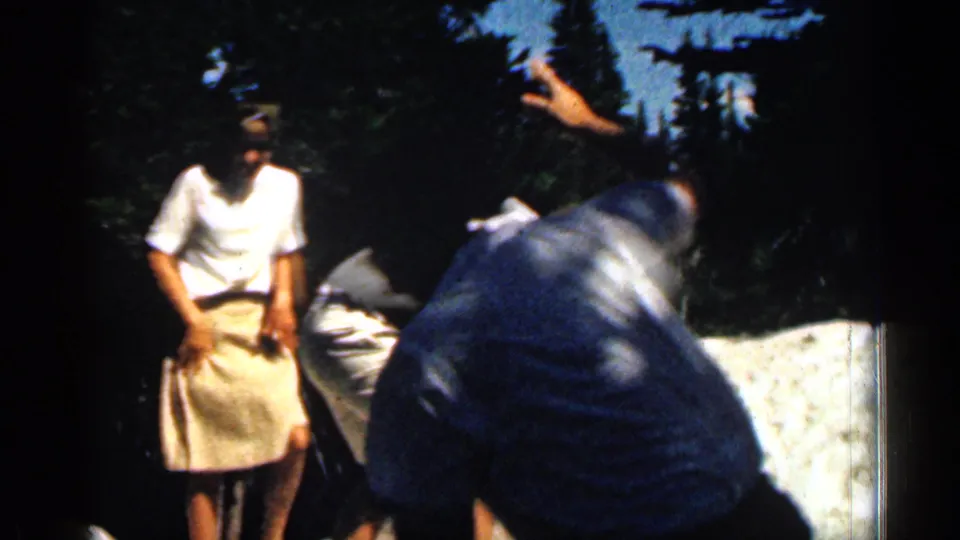 A woman in a light skirt stands beside men climbing over rocks during a 1963 Colorado outdoor home movie.