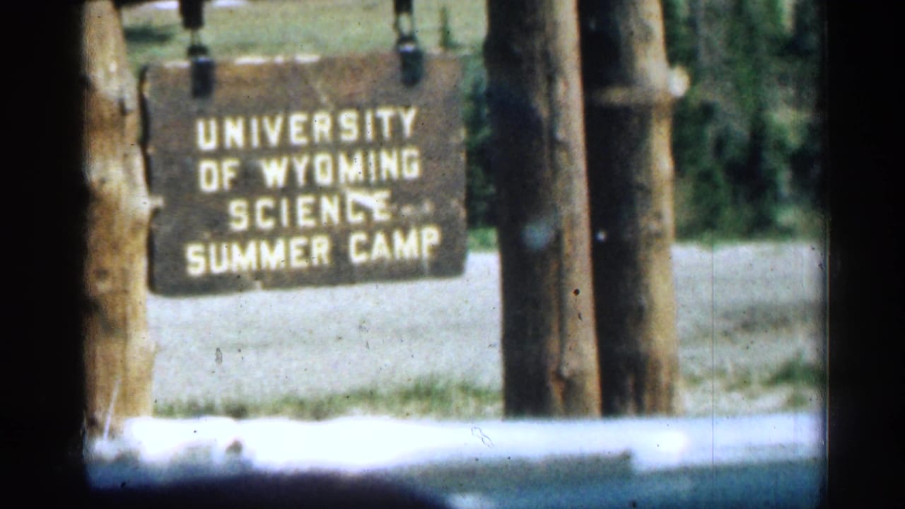 1963 Colorado 8mm frame showing a wooden University of Wyoming Science Summer Camp sign near a roadside or camp entrance.