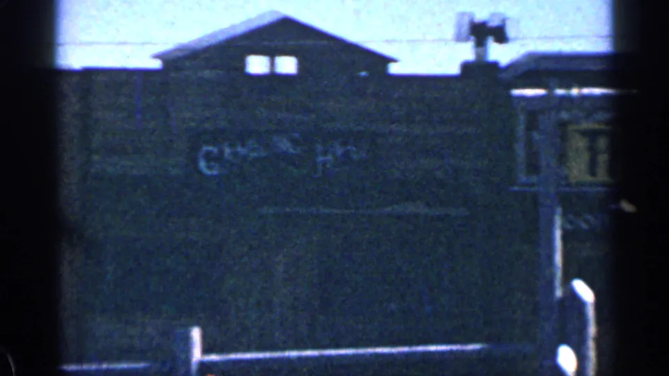 Grainy 1963 Colorado frame showing a shadowed building facade with faint lettering and a gabled roofline.