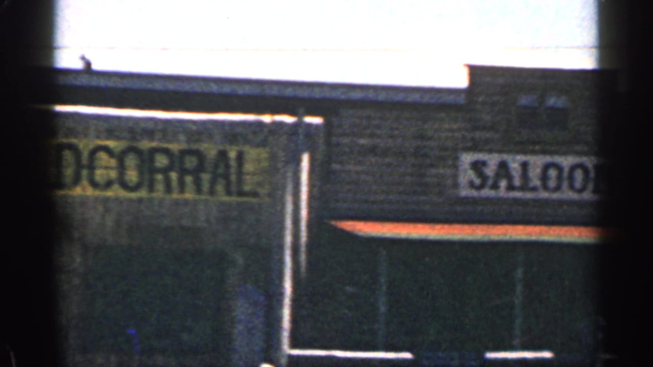 1963 Colorado 8mm frame showing a partial The Old Corral sign on a rustic roadside facade beneath bright sky and hills.