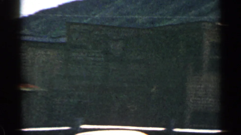 1963 Colorado 8mm view of a rustic facade with a partial saloon sign, dark window openings, and a hillside backdrop.
