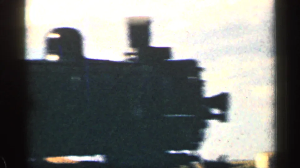 Close 8mm view of a steam locomotive front and smokestack in silhouette, with bright sky behind it.