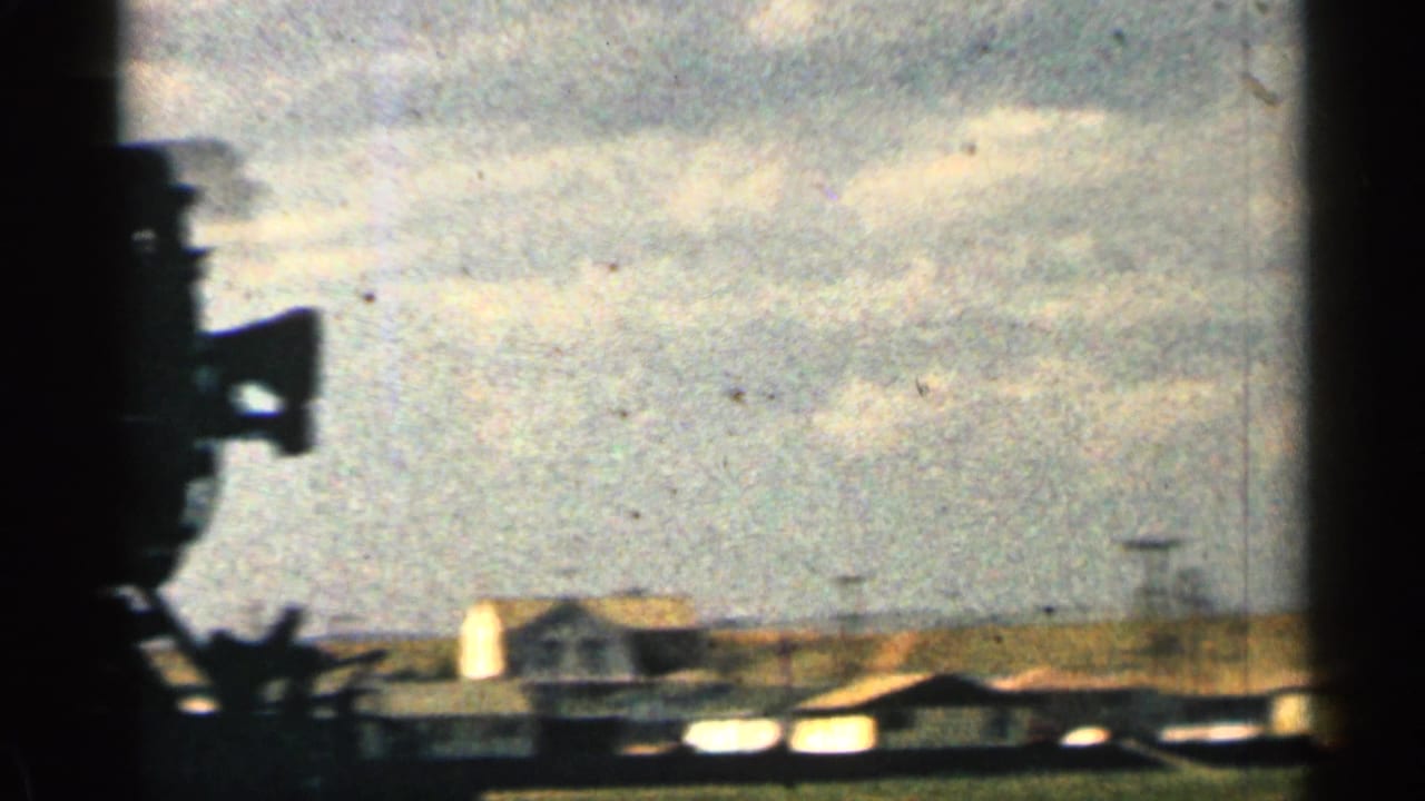 1963 Colorado 8mm frame showing a cloudy sky, low rural structures, and a dark foreground silhouette at the left edge.