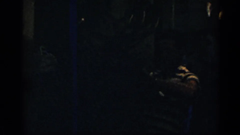 Dim 8mm interior view from the Colorado home movie, with an indistinct person in a striped shirt partly visible in shadow.