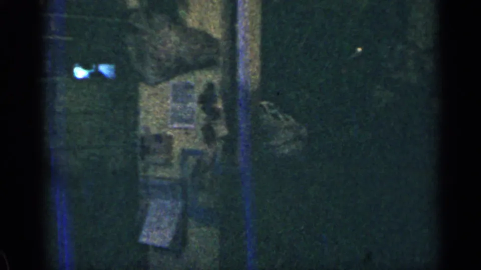 Low-light 1963 Colorado home-movie frame showing a shadowed wall area with papers or small objects and visible blue film streaking.