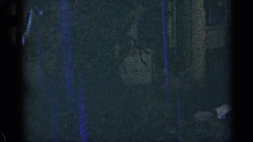Dark interior 8mm frame with a textured wall surface, blue vertical streaks, and a small bright object near the lower right.
