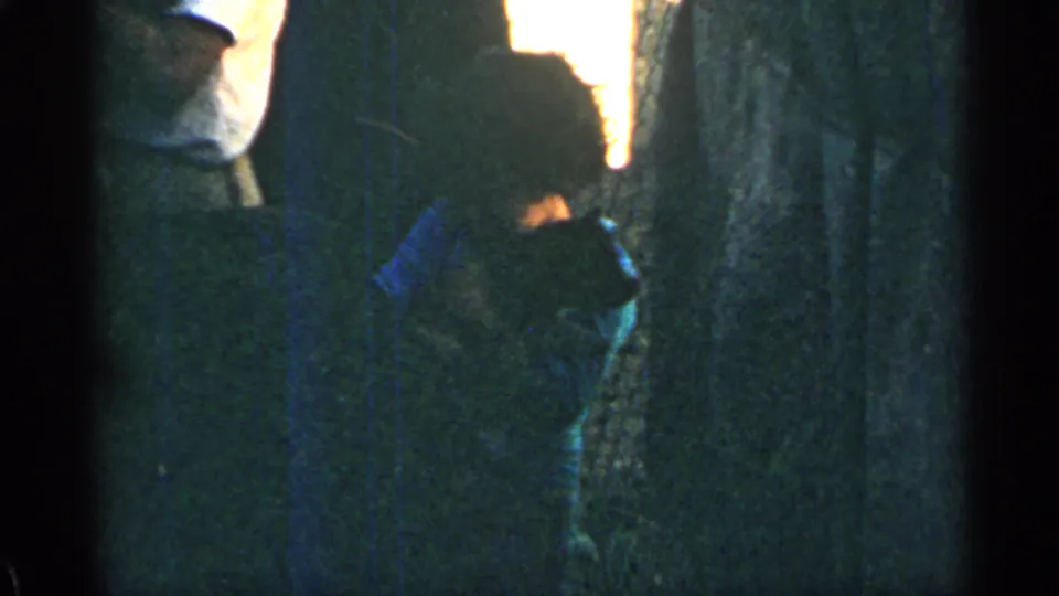 Low-light 1963 Colorado home-movie frame showing a partial adult figure beside the interior wall and taxidermy display.