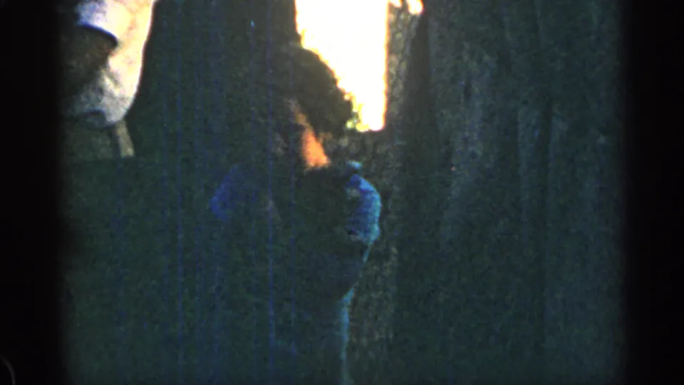In this 1963 Colorado home-movie frame, the child shifts position with the puppy against a wooded background.