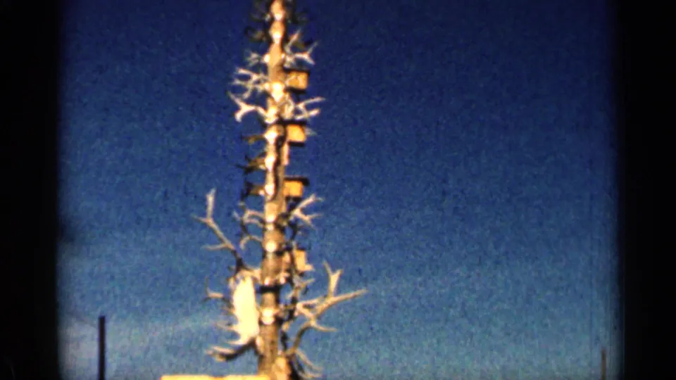 1963 Colorado 8mm frame isolating the upper part of an antler-covered wooden tower beneath clear sky.