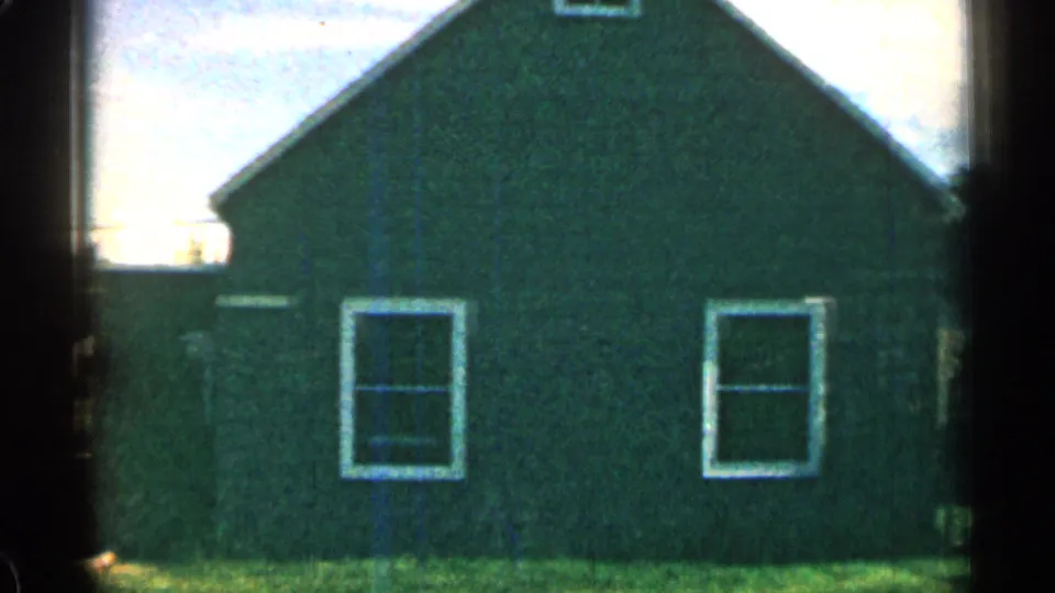 Close 1963 Colorado home-movie view of a green house exterior with two white-trimmed windows and lawn in the foreground.