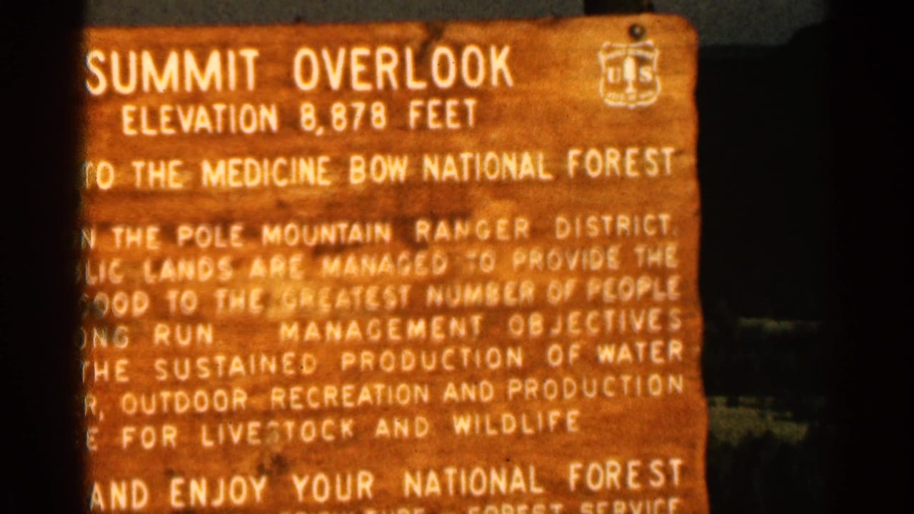 Closer 1963 view of the Summit Overlook sign, showing elevation text, forest service emblem, and management wording on a wooden board.