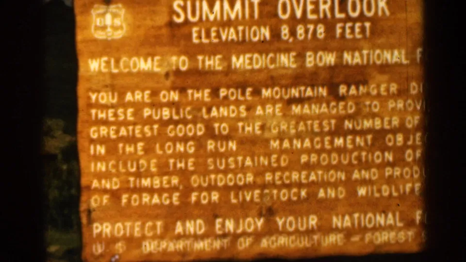 1963 frame of the Summit Overlook sign in Medicine Bow National Forest, with trees visible beside the wooden sign and soft 8mm focus.