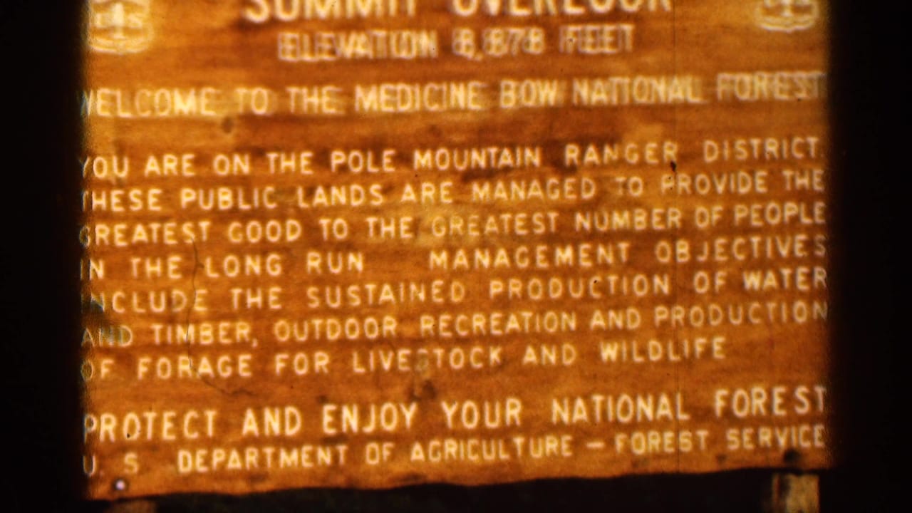 1963 Colorado 8mm frame showing a warm-lit Summit Overlook sign for Medicine Bow National Forest with elevation and ranger district text.
