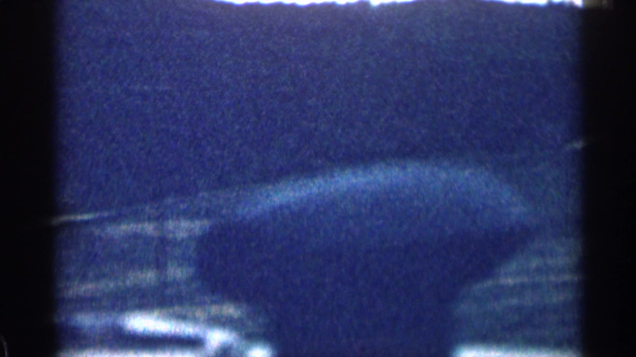 1963 Colorado home-movie view from inside a moving vehicle, showing dark hills, open ground, and bright sky through shadowed frame edges.