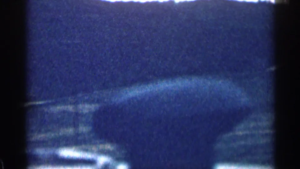 1963 Colorado home-movie view from inside a moving vehicle, showing dark hills, open ground, and bright sky through shadowed frame edges.
