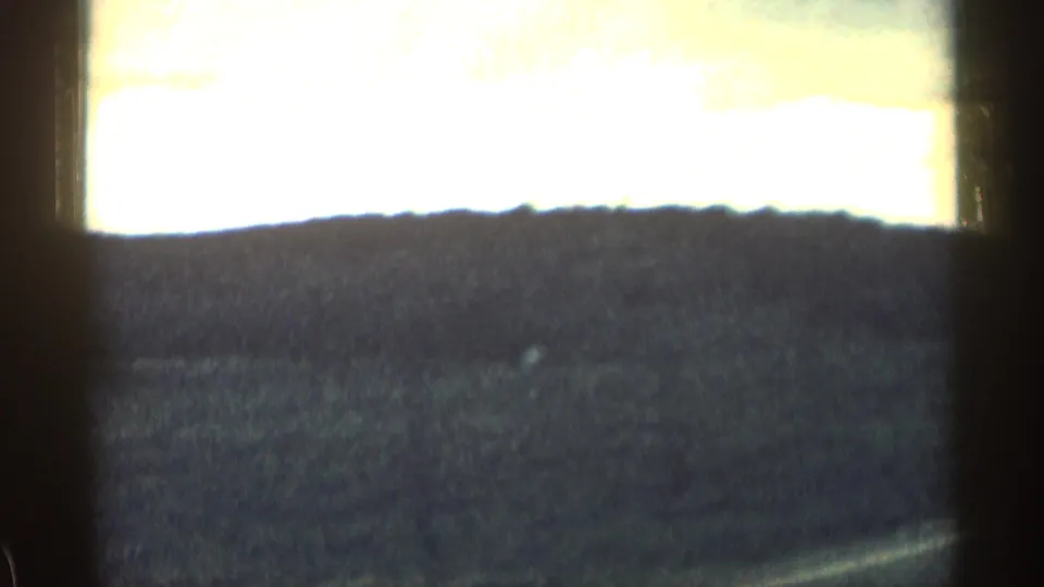 1963 Colorado road-view frame with a bright band of sky, dark ridgeline, open field, and vehicle interior shadows along the edges.