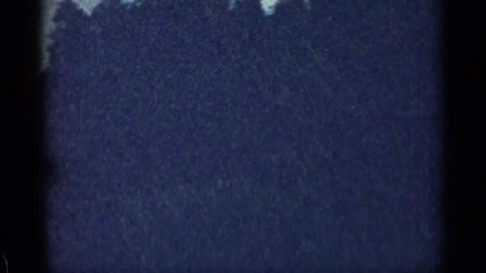 Dark, grainy end frame from a 1963 Colorado vehicle-view clip, with faint landscape detail and shadowed film edges visible.