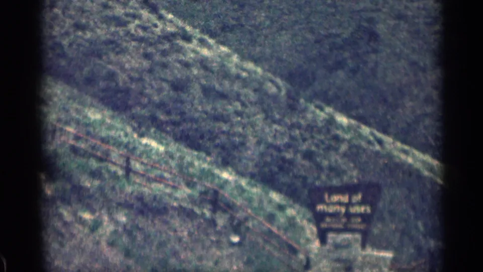 1963 Colorado 8mm frame with a roadside lodging sign, wooded hillside, and washed color from the moving camera view.