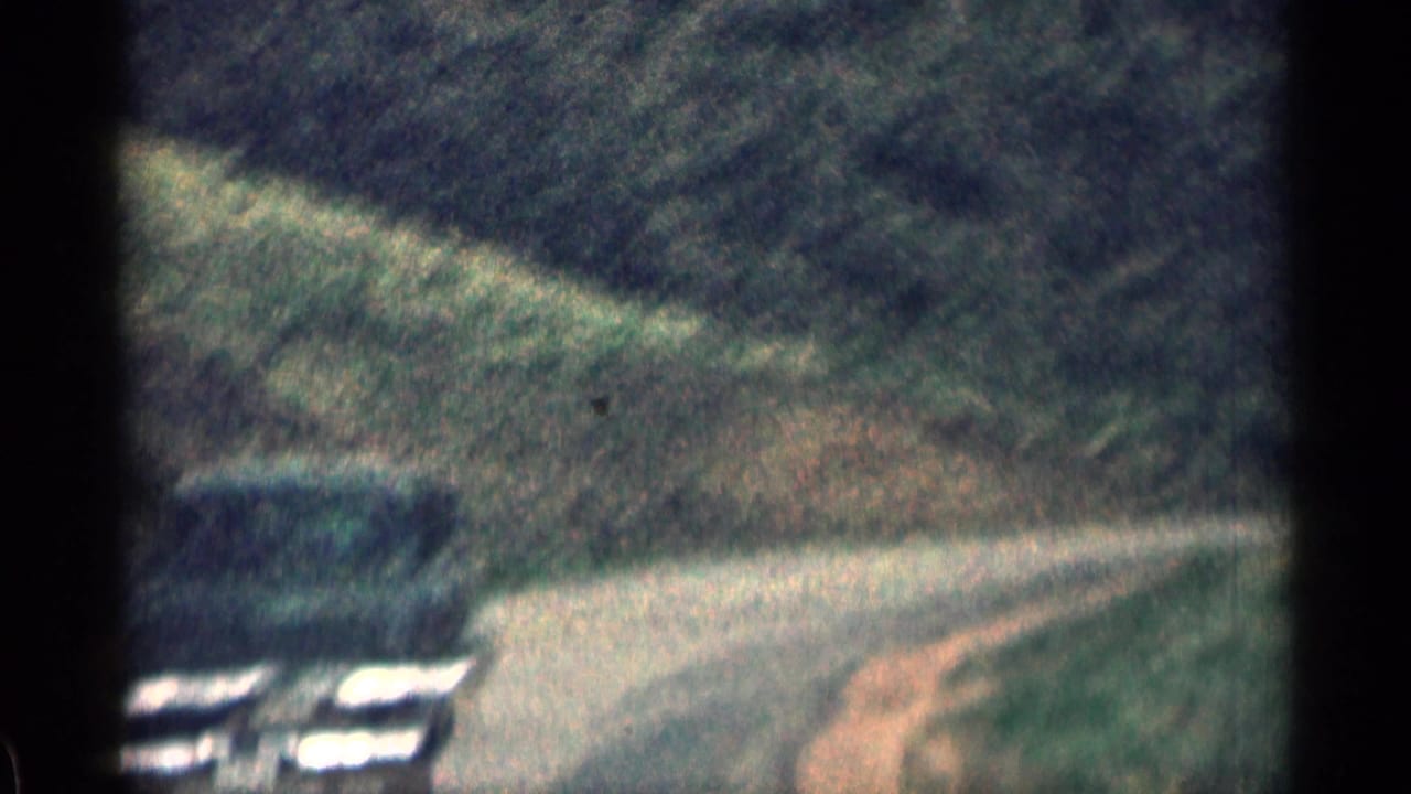 Curving mountain road with a light-colored car near the bend.