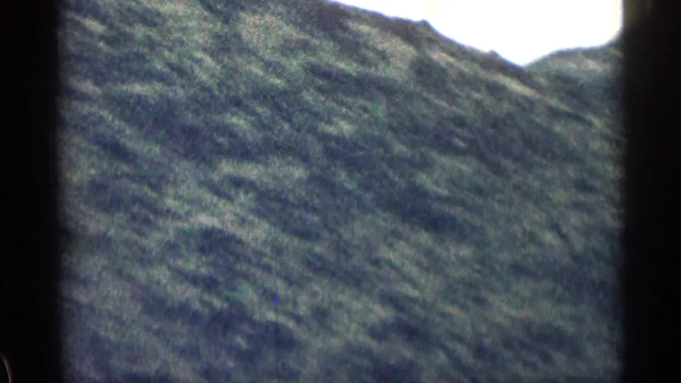 A soft, grainy 8mm view of a steep grassy Colorado hillside, filmed from a moving road-trip perspective in the supplied 1963 clip.