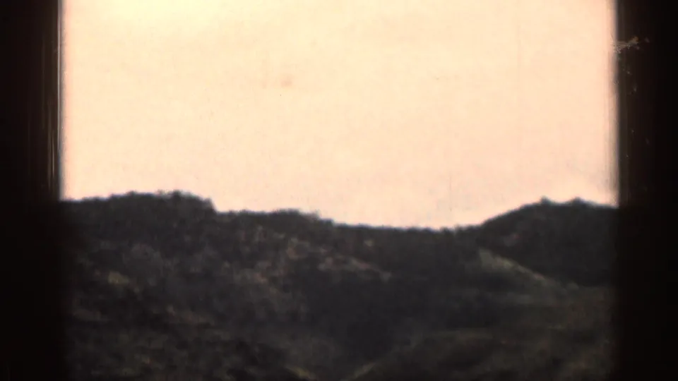 Faded 8mm view of Colorado hills with a distant ridge, dark foreground slope, and pale sky.