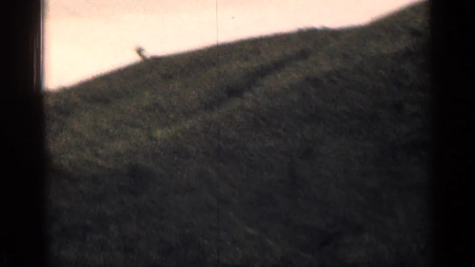 1963 Colorado 8mm frame showing a dark green hillside and a small indistinct shape near the skyline.