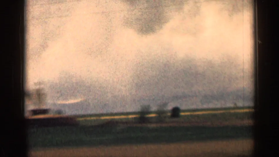 Grainy 1963 Colorado home-movie frame with a distant hillside shape beyond open roadside land.