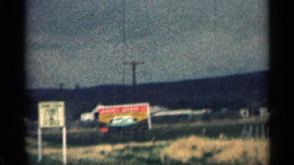 1963 Colorado 8mm frame showing a roadside junction sign area, utility pole, low buildings, and dry grass.