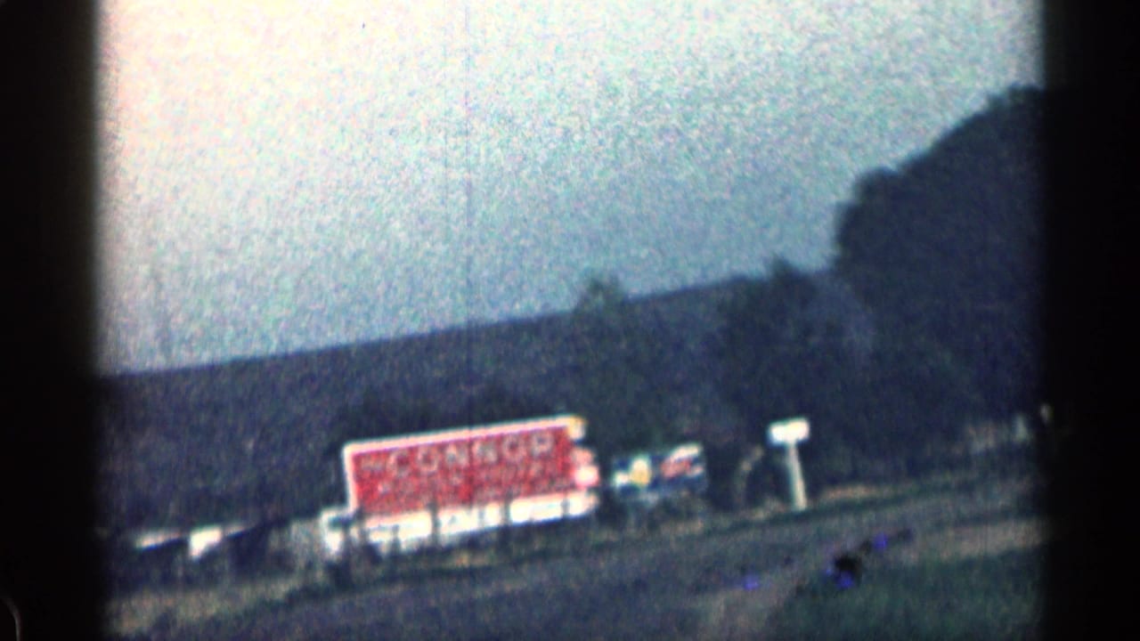 Roadside buildings and a red sign below a dark hillside.