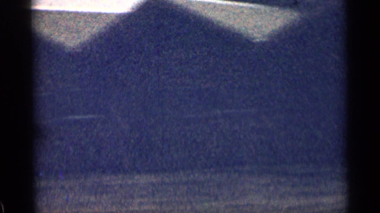 Soft 8mm view of a dark Colorado hillside with faint roadside detail and heavy film grain.