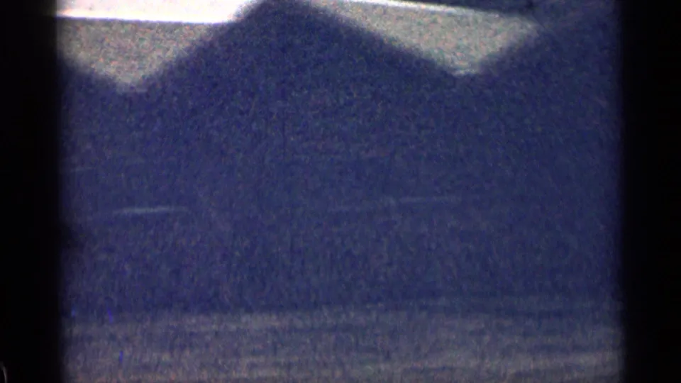Soft 8mm view of a dark Colorado hillside with faint roadside detail and heavy film grain.