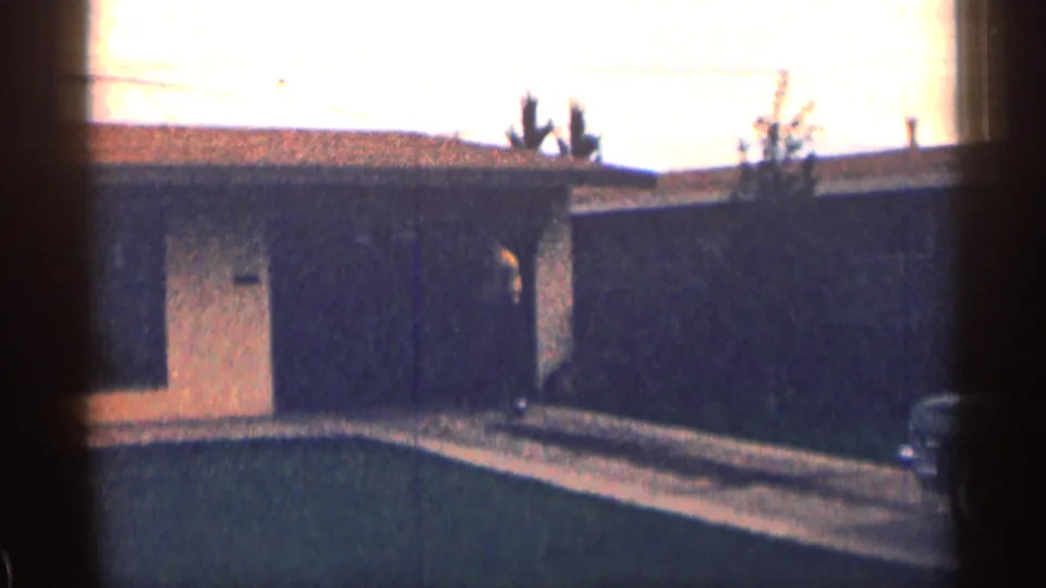 1963 Colorado 8mm frame showing a low suburban house, front door, lawn, driveway, roofline cacti, and a partly visible person.