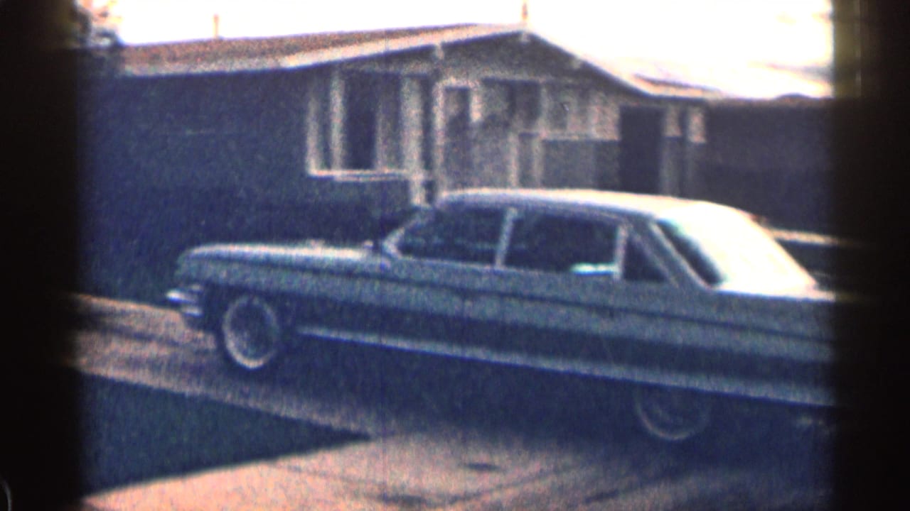 Classic sedan parked beside a low suburban house and driveway.