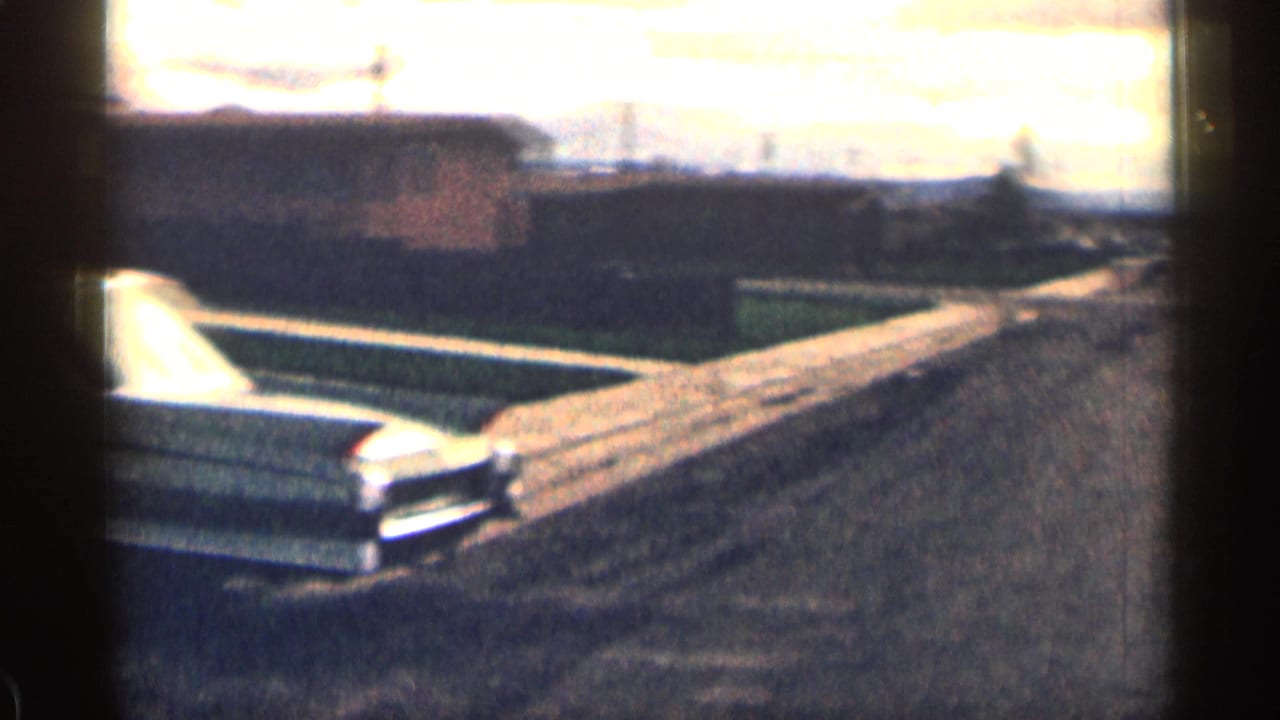 Rear angle of a classic sedan by a residential driveway in a quiet Colorado suburb, filmed on 8mm in 1963.
