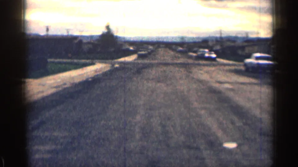 1963 Colorado suburban street view with low houses, sidewalks, distant parked cars, and soft 8mm exposure.