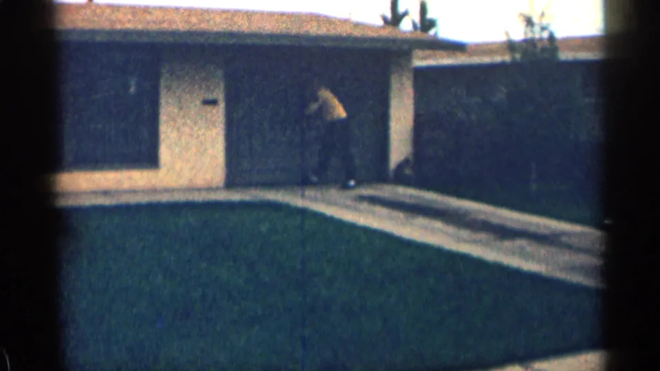 A person stands near the entrance of a single-story suburban house with lawn and walkway in 1963 Colorado footage.