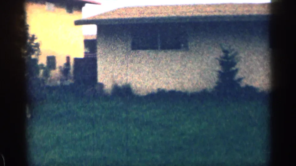 1963 Colorado home-movie view of a low residential building, lawn, shrub growth, and neighboring structures at the edge of the frame.