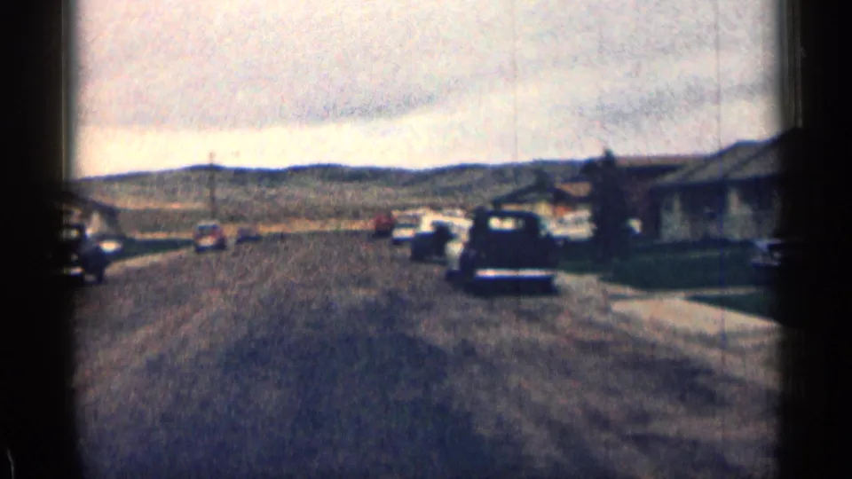 Wide 1963 Colorado street view from an 8mm home movie, showing parked vehicles, ranch-style homes, sidewalks, lawns, and distant hills.
