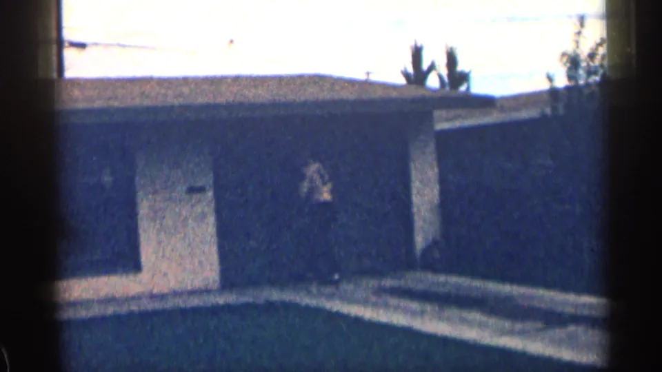 1963 Colorado frame showing the garage wall and door from a handheld 8mm view, with driveway pavement and roofline visible.