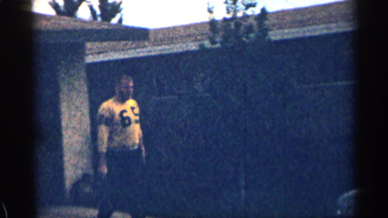 Man in a yellow number 69 jersey stands near the wall of a house.