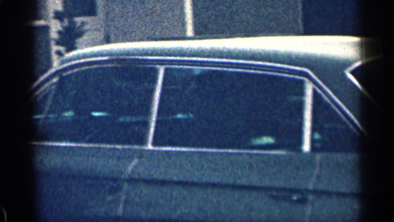 Close view of a dark vintage sedan beside a building or driveway.
