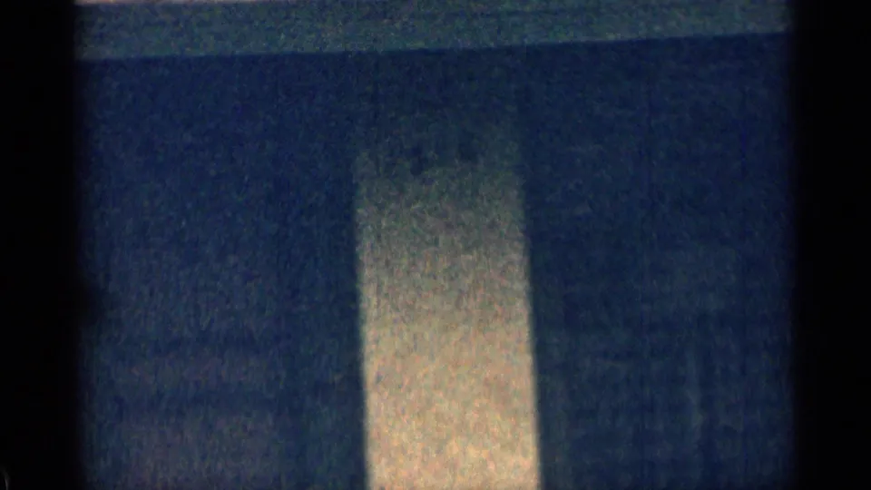 Soft 8mm frame of a residential exterior detail, showing a pale vertical wall or column against darker siding.
