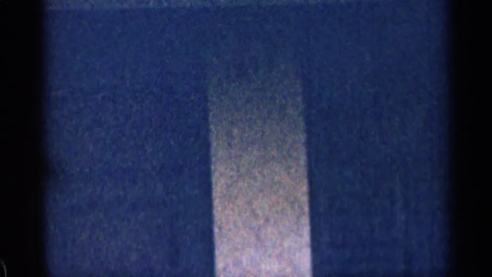 Grainy 1963 Colorado home-movie frame with a pale vertical house detail and dark surrounding wall area.