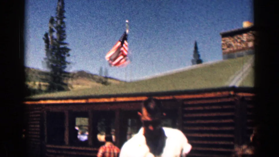 1963 Colorado 8mm frame with an American flag above a log cabin and visitors gathered near the entrance.