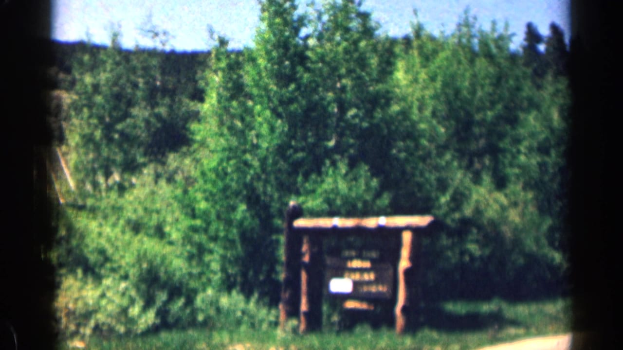 Colorado mountain visitor area with a wooden information kiosk or signboard surrounded by summer trees.