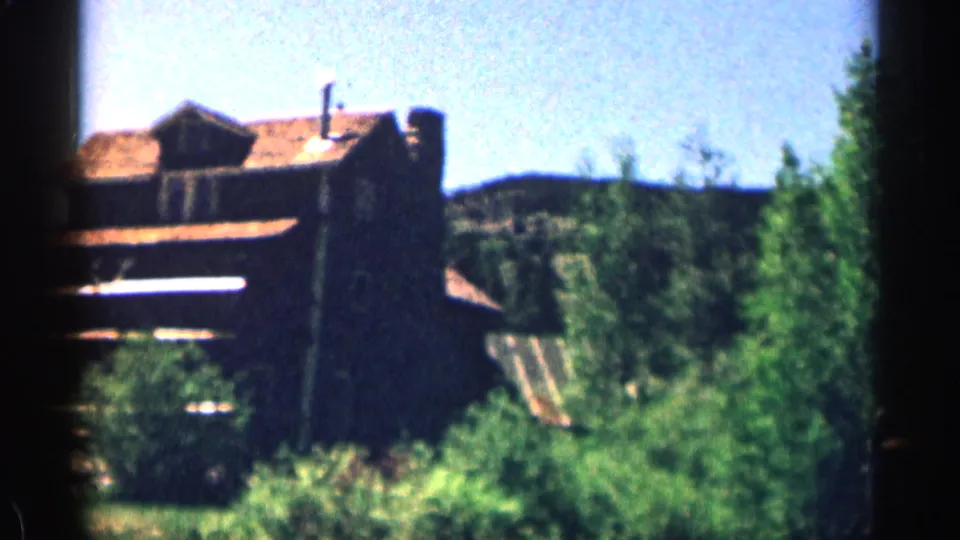 1963 Colorado home-movie view of a rustic lodge-like building seen through trees in a mountain setting.