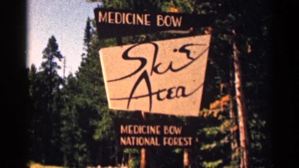 Handheld 8mm view of the Medicine Bow Ski Area sign, with national forest text and tall trees behind it.