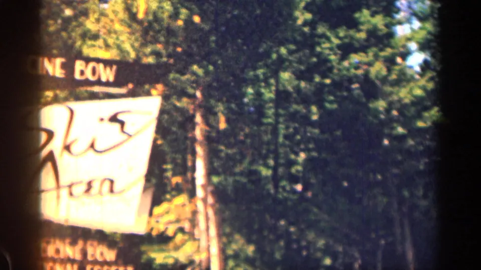 Partial sign reading Medicine Bow appears at the edge of a wooded roadside in 1963 8mm footage.