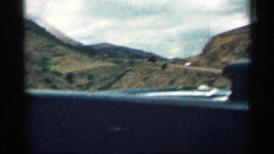 From inside a moving car, the frame looks toward Colorado hills and road edges, with dashboard detail dark across the foreground.