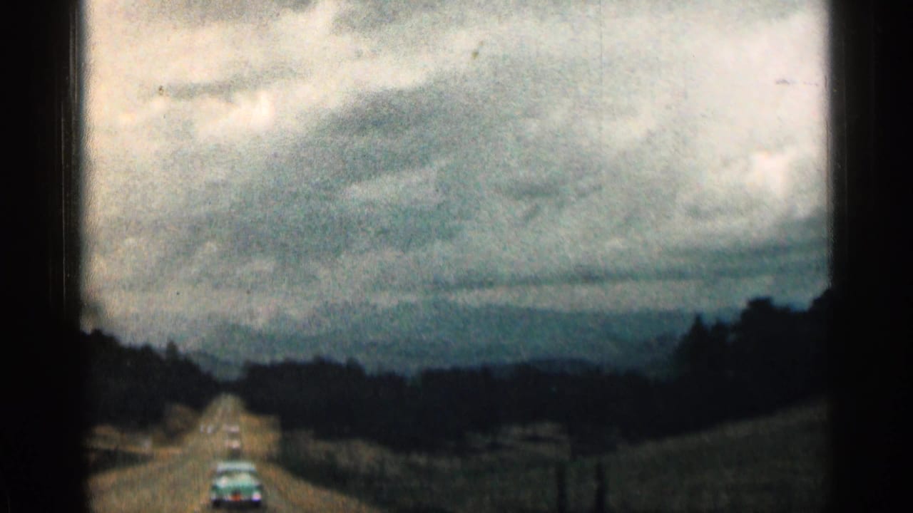 Two-lane road seen from a moving car under a cloudy sky with dark hills ahead.